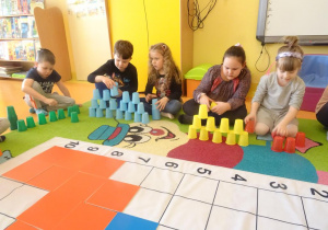 Dzieci układają z kolorowych kubków plastikowych trzy wieże.